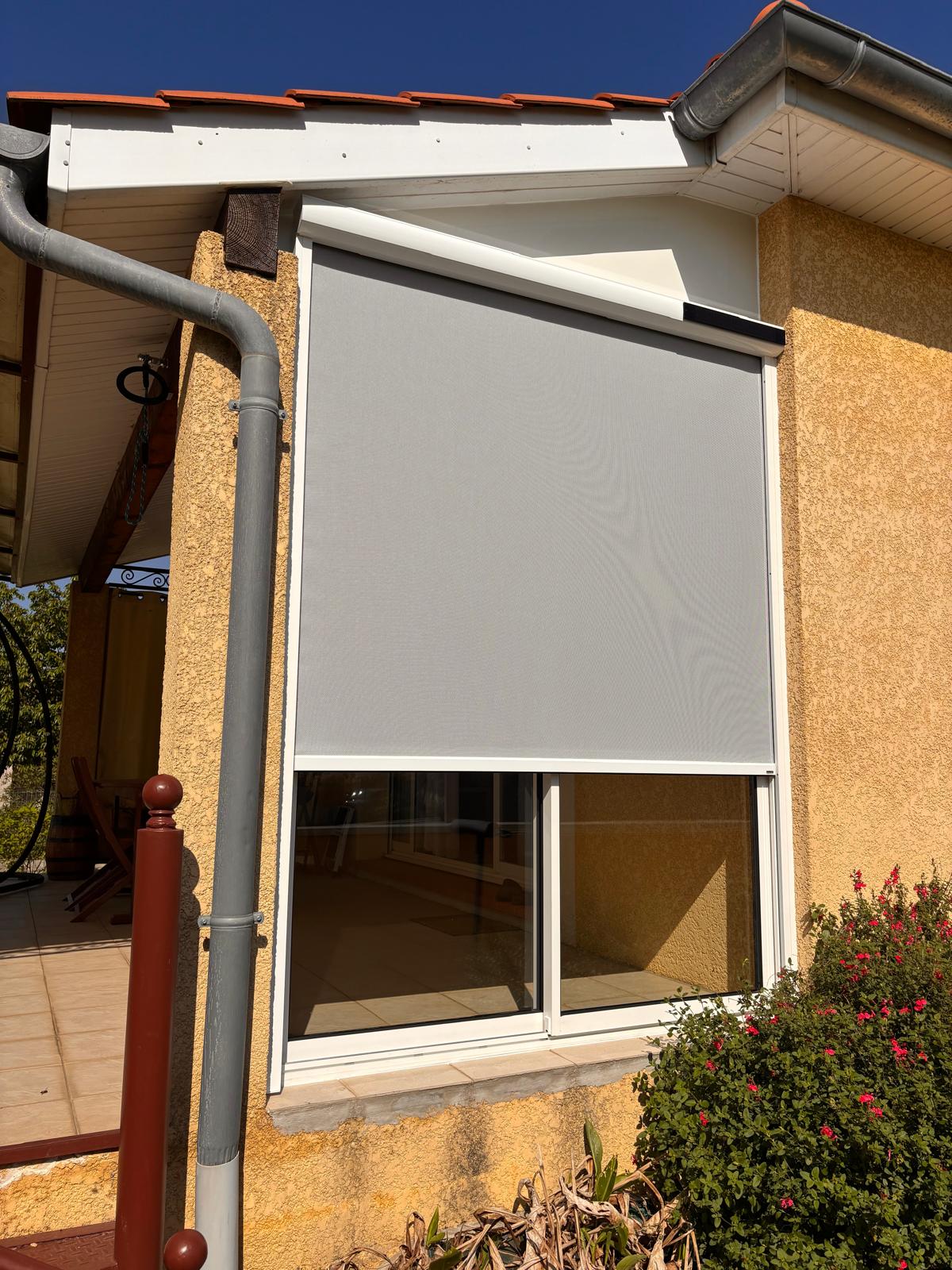 vue de l'extérieur d'une fenêtre coulissante installée et de son store screen anti-vent qui filtre les rayons du soleil