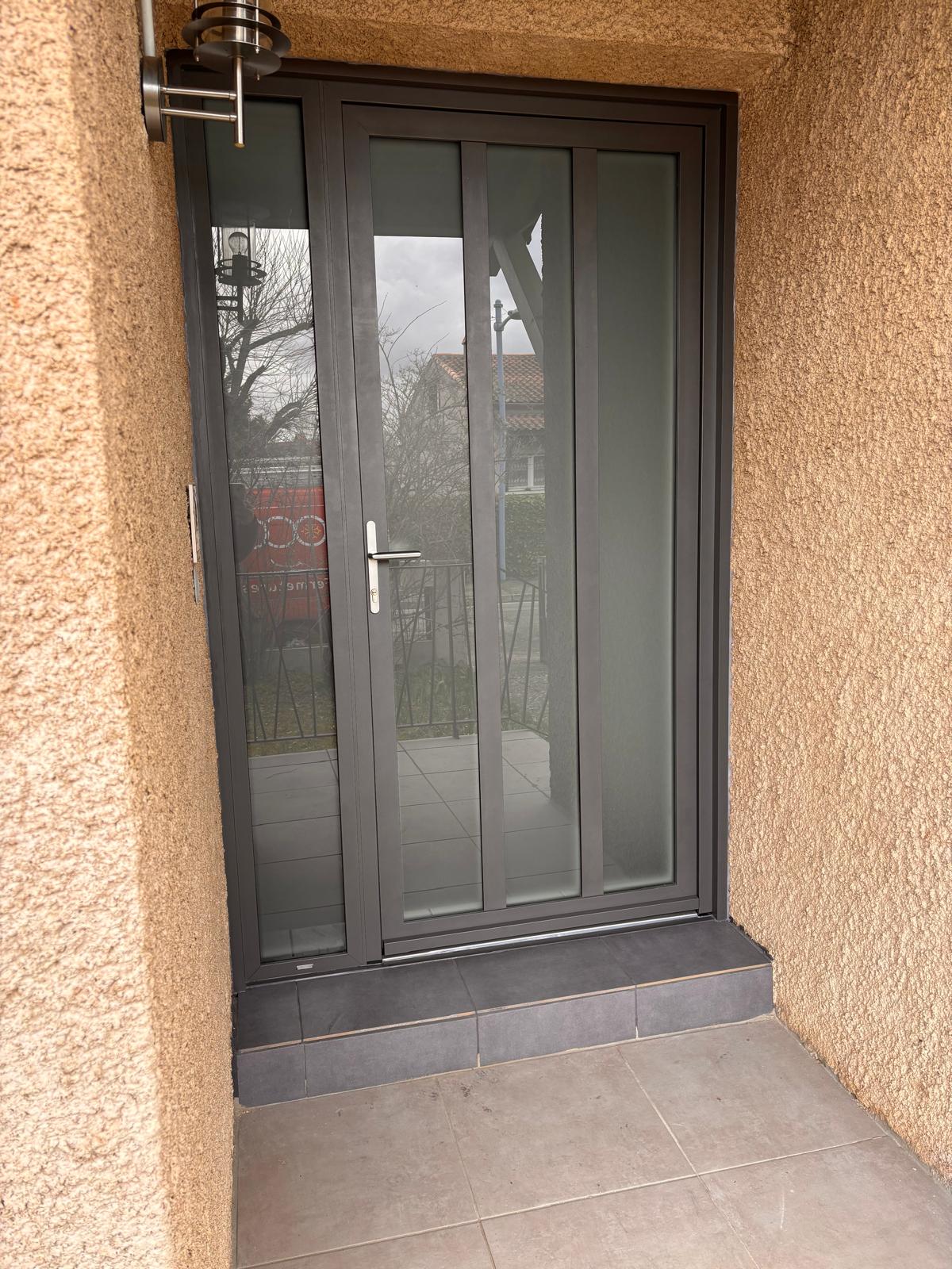 photo d'une porte d'entrée en alu gris sablé à l'extérieur
