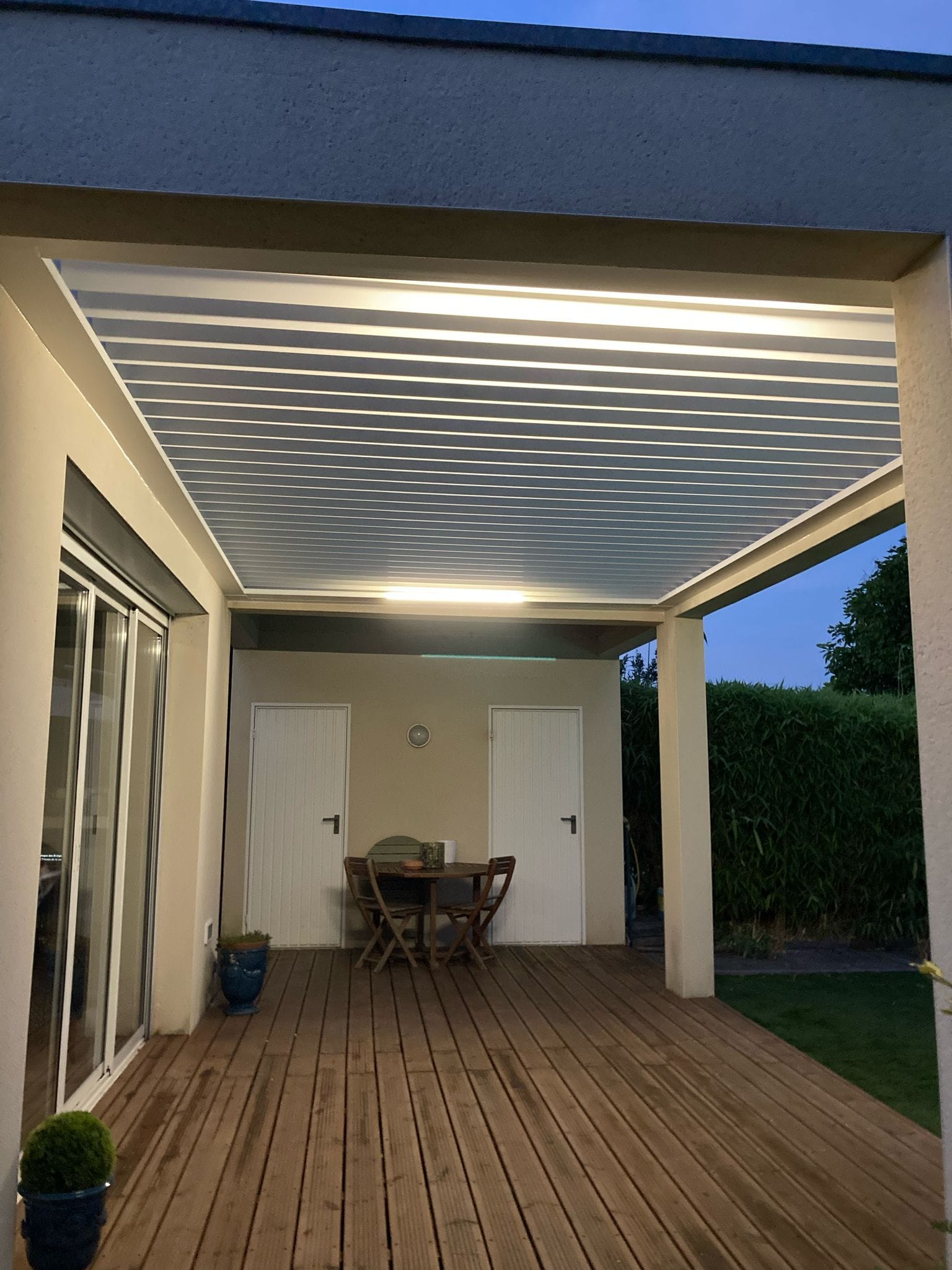 vue de nuit d'une pergola bioclimatique avec lames ouvertes, installée entre des murs à Toulouse par Occ'Fermetures