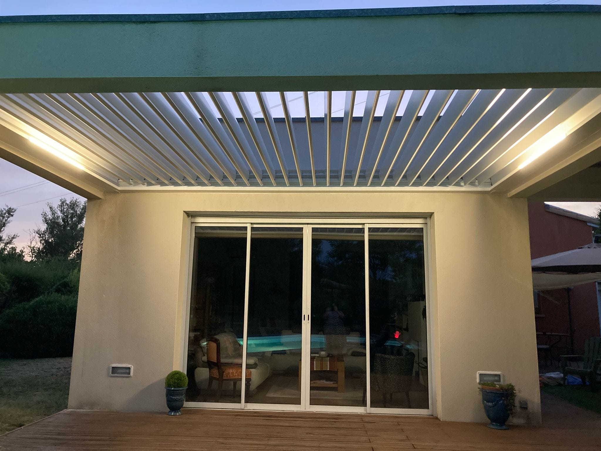 vue de face et de nuit avec éclairage led d'une pergola bioclimatique avec lames ouvertes, installée entre des murs à Toulouse par Occ'Fermetures